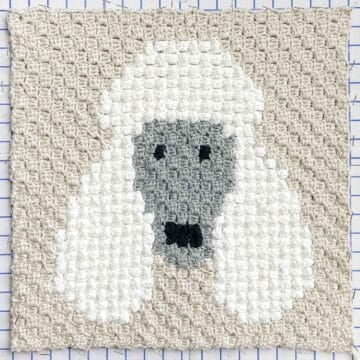 An overhead view of a corner to corner crochet poodle made with white yarn and popcorn bobble stitches.