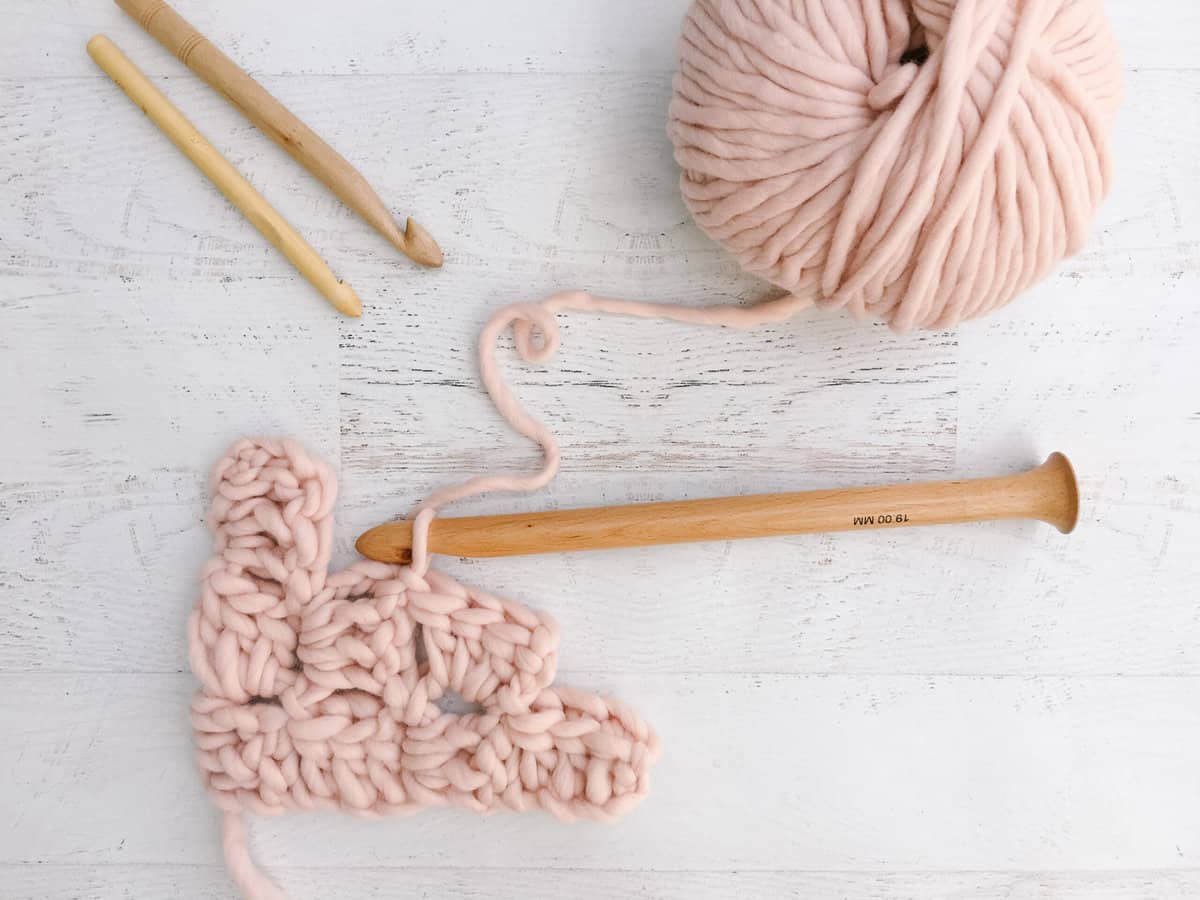 Chunky pink wool yarn and a thick wood hook being used to demonstrate the first few rows of corner to corner crochet.