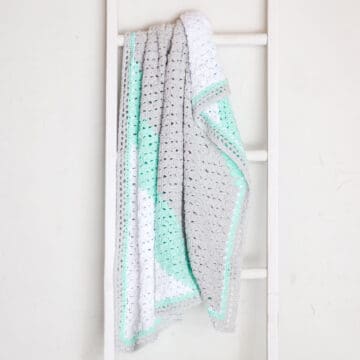 A corner to corner crochet blanket hanging on a ladder.