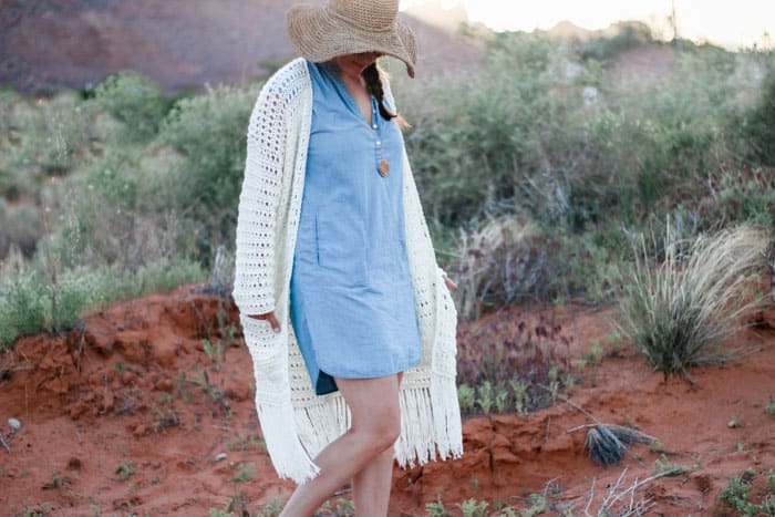 A woman standing in the desert wearing a long crochet cardigan with fringe.