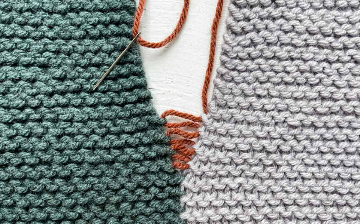 Knit garter stitch stripes being sewed together with orange yarn.
