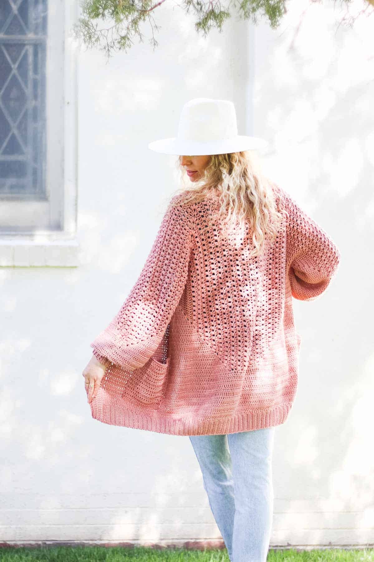 View from the back of a blonde woman wearing a linen dress and a crochet hexagon cardigan made with Lion Brand Coboo in the color "Mauve."
