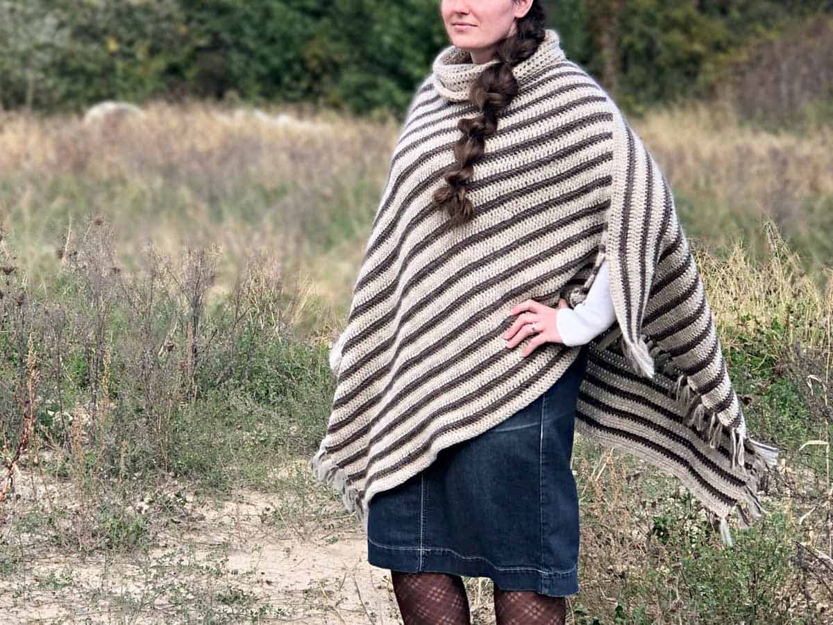 Woman wearing a crochet poncho with fringe standing in an open field.